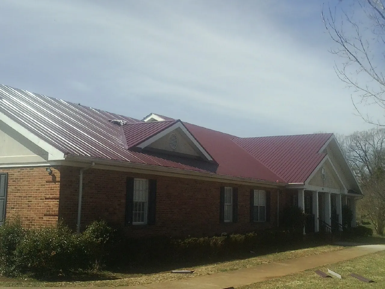 Red metal roof with gabled entries on a long brick building, from a Hail Damage Roof Repair job in Bonduel