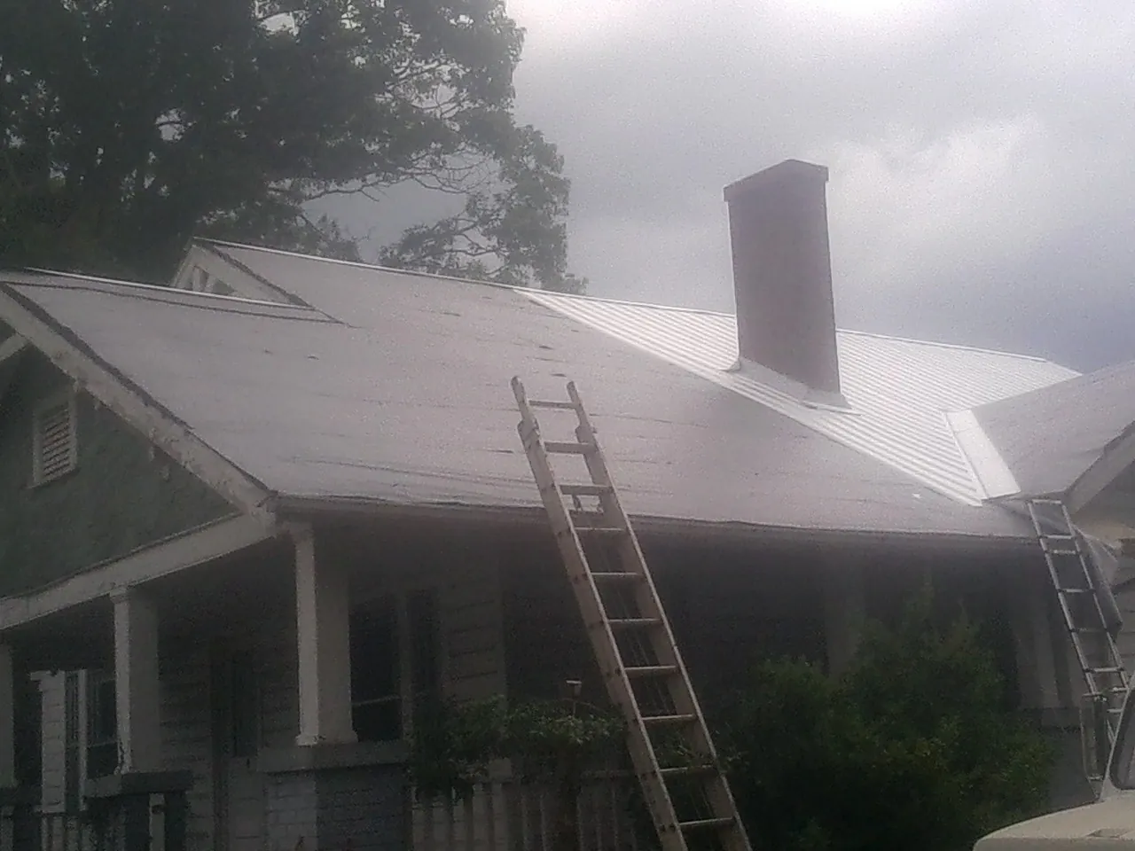 Ladders against a metal roof on an older home with a brick chimney in Bonduel
