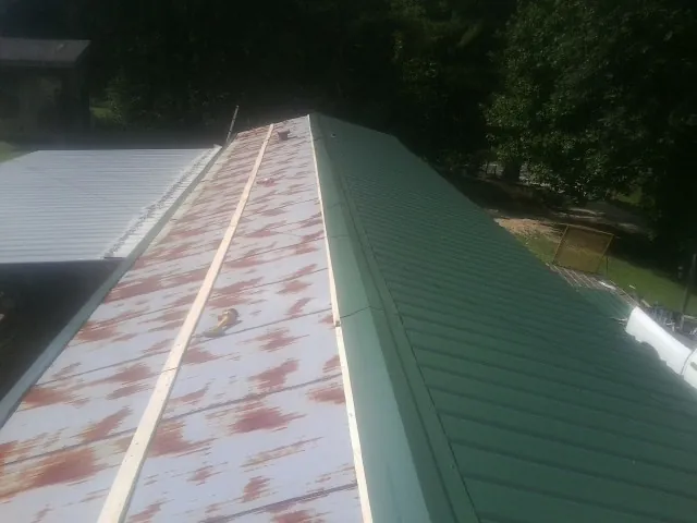 Old rusted panels beside newly installed green metal roofing — Wind Damage Roof Repair by Roofing Brothers in Bonduel