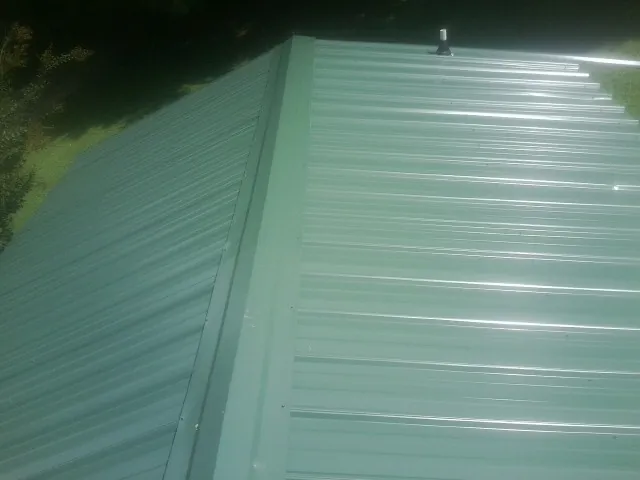 New green metal panels meeting at the ridge of a roof — Flat Roof Repair work by our crew in Bonduel