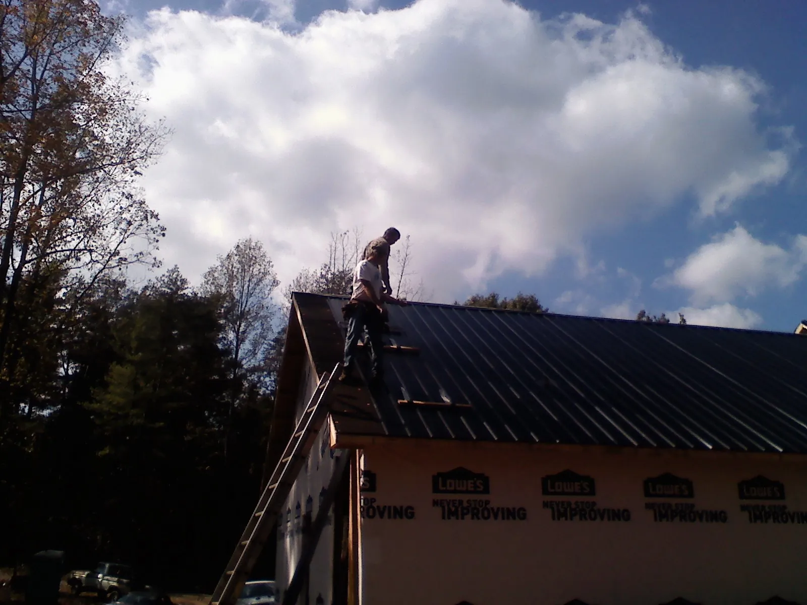Roofer fastening dark metal panels high against a cloudy sky, from a Roof Inspection job in Bonduel