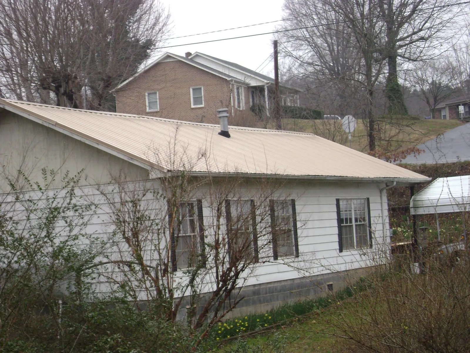 Tan metal roof on a white sided house set into a hillside — Commercial Roofing by Roofing Brothers in Bonduel