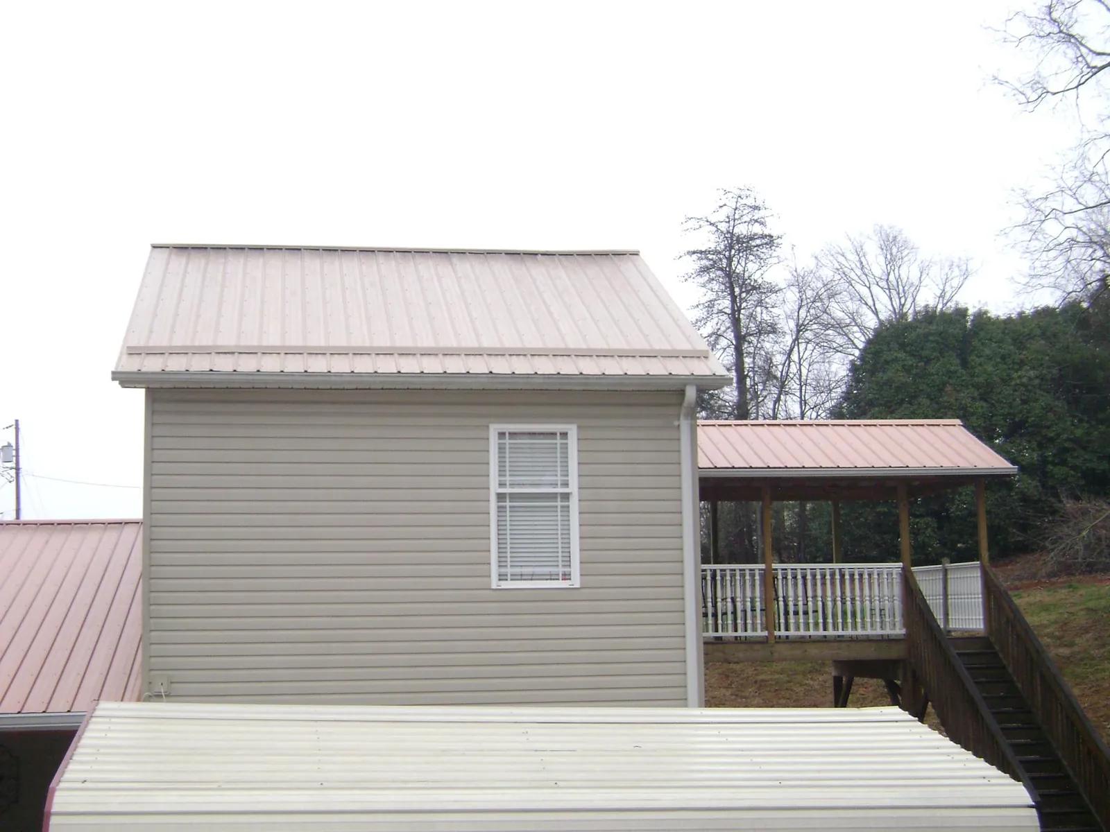 Tan metal roofs on a two story addition and attached porch, from a Roof Replacement job in Bonduel